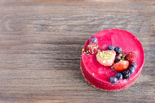 Taze çilek, ahududu, yaban mersini, kuş üzümü ve ahşap zemin üzerine Antep fıstığı ile lezzetli frambuazlı pasta. metniniz için boş alan.