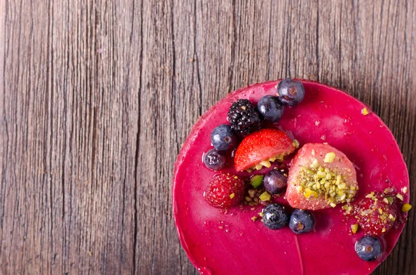 Taze çilek, ahududu, yaban mersini, kuş üzümü ve ahşap zemin üzerine Antep fıstığı ile lezzetli frambuazlı pasta. metniniz için boş alan.