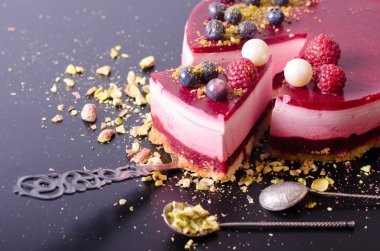 Taze çilek, ahududu, yaban mersini, kuş üzümü ve siyah arka plan üzerine Antep fıstığı ile lezzetli frambuazlı pasta. 