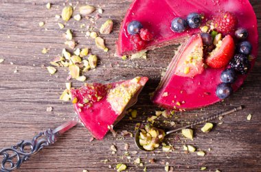 Taze çilek, ahududu, yaban mersini, kuş üzümü ve ahşap zemin üzerine Antep fıstığı ile lezzetli frambuazlı pasta.