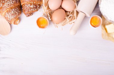 Kruvasan pişirme için Malzemeler - un, tahta kaşık, oklava, yumurta, yumurta sarısı, tereyağı beyaz arka plan üzerinde servis.