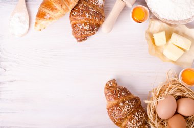 Kruvasan pişirme için Malzemeler - un, tahta kaşık, oklava, yumurta, yumurta sarısı, tereyağı beyaz arka plan üzerinde servis.