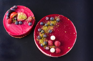 Taze çilek, ahududu, yaban mersini, kuş üzümü ve siyah arka plan üzerine Antep fıstığı ile iki lezzetli kek. Metniniz için boş alan.