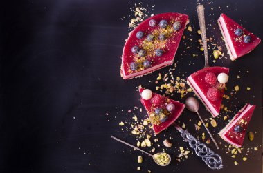 Taze çilek, ahududu, yaban mersini, kuş üzümü ve siyah arka plan üzerine Antep fıstığı ile lezzetli frambuazlı pasta parçaları. Metniniz için boş alan.