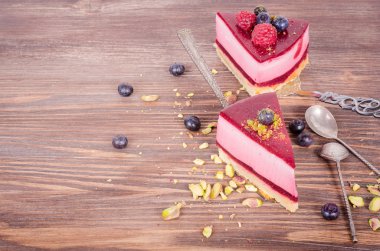 Taze ahududu, yaban mersini, kuş üzümü ve kürek, ahşap arka plan üzerinde Antep fıstığı ile lezzetli frambuazlı pasta parçası. Metniniz için boş alan.