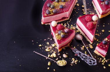 Taze çilek, ahududu, yaban mersini, kuş üzümü ve siyah arka plan üzerine Antep fıstığı ile lezzetli frambuazlı pasta parçaları. Metniniz için boş alan.