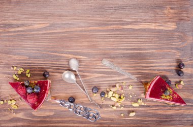 Taze ahududu, yaban mersini, kuş üzümü ve kürek, ahşap arka plan üzerinde Antep fıstığı ile lezzetli frambuazlı pasta parçası. Metniniz için boş alan.