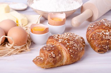 Kruvasan pişirme için Malzemeler - un, tahta kaşık, oklava, yumurta, yumurta sarısı, tereyağı beyaz arka plan üzerinde servis.