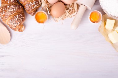 Kruvasan pişirme için Malzemeler - un, tahta kaşık, oklava, yumurta, yumurta sarısı, tereyağı beyaz arka plan üzerinde servis.