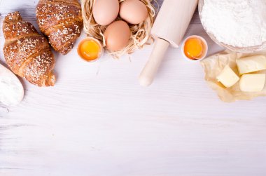 Kruvasan pişirme için Malzemeler - un, tahta kaşık, oklava, yumurta, yumurta sarısı, tereyağı beyaz arka plan üzerinde servis.