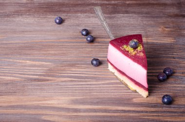 Taze ahududu, yaban mersini, kuş üzümü ve kürek, ahşap arka plan üzerinde Antep fıstığı ile lezzetli frambuazlı pasta parçası. Metniniz için boş alan.