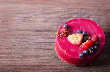 Taze çilek, ahududu, yaban mersini, kuş üzümü ve ahşap zemin üzerine Antep fıstığı ile lezzetli frambuazlı pasta. metniniz için boş alan.