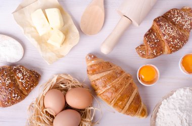 Kruvasan pişirme için Malzemeler - un, tahta kaşık, oklava, yumurta, yumurta sarısı, tereyağı beyaz arka plan üzerinde servis.