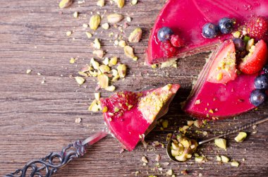 Taze çilek, ahududu, yaban mersini, kuş üzümü ve ahşap zemin üzerine Antep fıstığı ile lezzetli frambuazlı pasta.