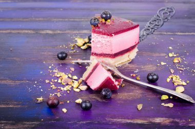 Taze ahududu, yaban mersini, kuş üzümü ve kürek, parlak mor, violet arka plan üzerinde Antep fıstığı ile lezzetli frambuazlı pasta parçası. Metniniz için boş alan.