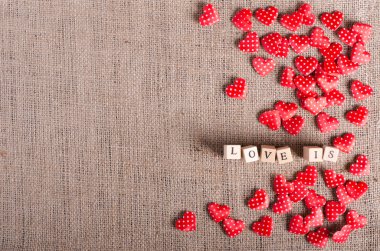 Aşk kelimesi tahta küplerde ve birçok kırmızı dekoratif kalpte çuval bezinde, branda arka planda. Klasik stil.  