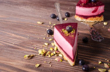 Taze ahududu, yaban mersini, kuş üzümü ve kürek, ahşap arka plan üzerinde Antep fıstığı ile lezzetli frambuazlı pasta parçası. Metniniz için boş alan.