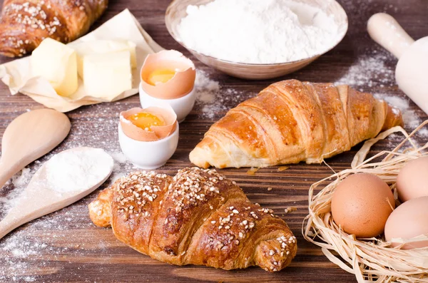 Zutaten zum Backen von Croissants - Papier, Mehl, Holzlöffel, Nudelholz, Eier, Eigelb, Butter, serviert auf einem rustikalen Holztisch. — Stockfoto