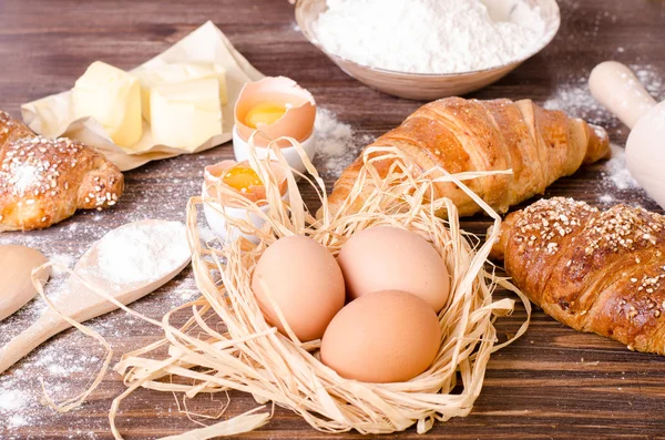 烤牛角面包的配料-纸, 面粉, 木勺, 滚针, 鸡蛋, 蛋黄, 黄油, 在一个简陋的木托盘桌上服务. — 图库照片