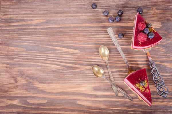 Piece of delicious raspberry cake with fresh raspberries, blueberry, currants and pistachios on shovel, wooden background. Free space for your text. — Stock Photo, Image