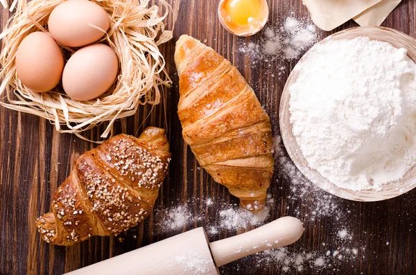 Zutaten zum Backen von Croissants - Papier, Mehl, Holzlöffel, Nudelholz, Eier, Eigelb, Butter, serviert auf einem rustikalen Holztisch. — Stockfoto