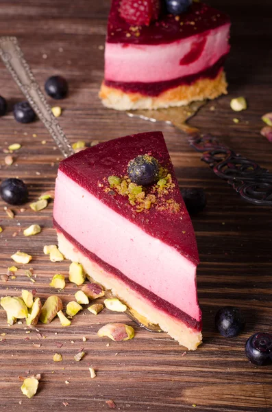 Stuk heerlijke frambozen cake met verse frambozen, bosbessen, krenten en pimpernoten (pistaches) op de schop, houten achtergrond. Vrije ruimte voor uw tekst. — Stockfoto