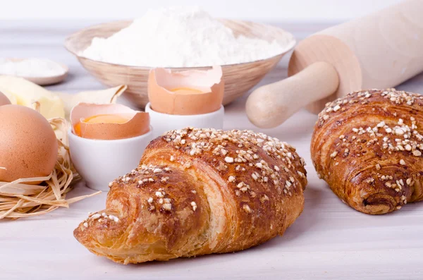 Kruvasan pişirme için Malzemeler - un, tahta kaşık, oklava, yumurta, yumurta sarısı, tereyağı beyaz arka plan üzerinde servis.