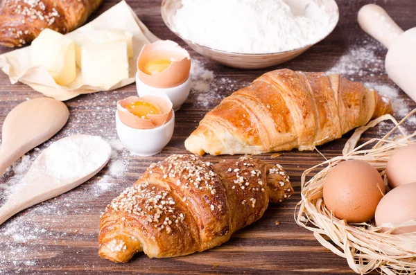 烤牛角面包的配料-纸, 面粉, 木勺, 滚针, 鸡蛋, 蛋黄, 黄油, 在一个简陋的木托盘桌上服务. — 图库照片