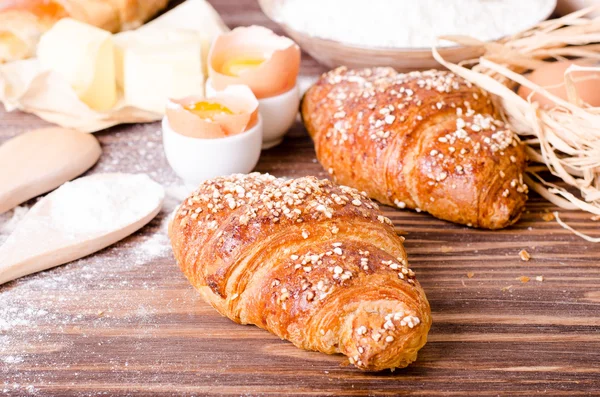 Ingredientes para hornear croissants: papel, harina, cuchara de madera, rodillo, huevos, yemas de huevo, mantequilla servida en una mesa rústica de bandeja de madera . — Foto de Stock