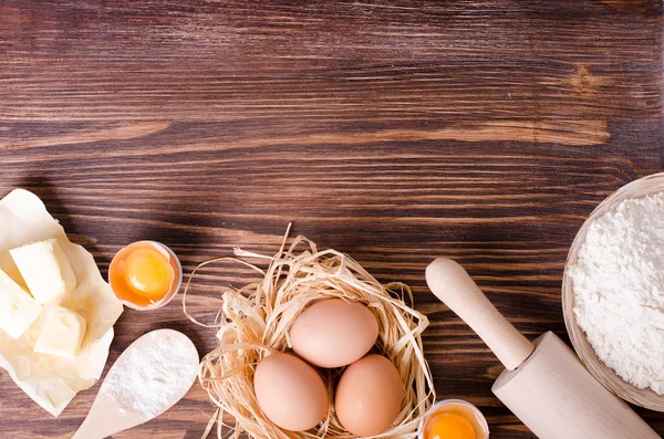Zutaten zum Backen - Mehl, Holzlöffel, Nudelholz, Eier, Eigelb, Butter auf einem Holztisch von oben. rustikaler Hintergrund mit freier Textfläche. — Stockfoto