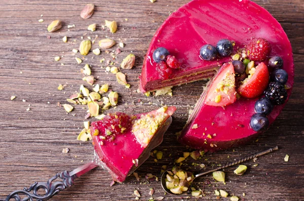 Delicious raspberry cake with fresh strawberries, raspberries, blueberry, currants and pistachios on wooden background. — Stock Photo, Image