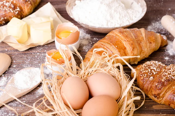 Zutaten zum Backen von Croissants - Papier, Mehl, Holzlöffel, Nudelholz, Eier, Eigelb, Butter, serviert auf einem rustikalen Holztisch. — Stockfoto