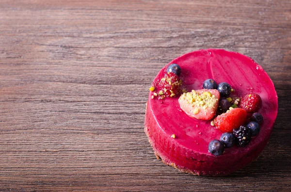 Taze çilek, ahududu, yaban mersini, kuş üzümü ve ahşap zemin üzerine Antep fıstığı ile lezzetli frambuazlı pasta. metniniz için boş alan.