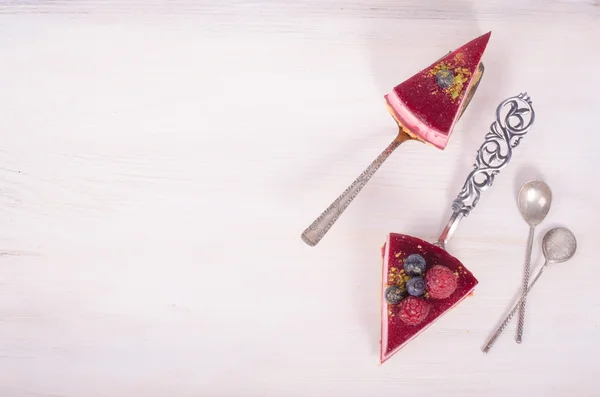 Piece of delicious raspberry cake with fresh raspberries, blueberry, currants and pistachios on shovel, white background. Free space for your text. — Stock Photo, Image