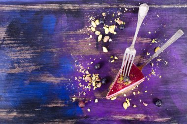 Taze ahududu, yaban mersini, kuş üzümü ve fıstık kürek, parlak mor, mor, mavi arka plan ile lezzetli frambuazlı pasta parçası. Metniniz için boş alan.