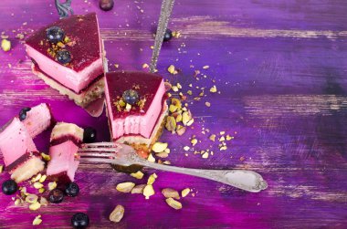 Taze ahududu, yaban mersini, kuş üzümü ve kürek, parlak mor, violet arka plan üzerinde Antep fıstığı ile lezzetli frambuazlı pasta parçası. Metniniz için boş alan.