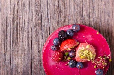 Taze çilek, ahududu, yaban mersini, kuş üzümü ve ahşap zemin üzerine Antep fıstığı ile lezzetli frambuazlı pasta. metniniz için boş alan.