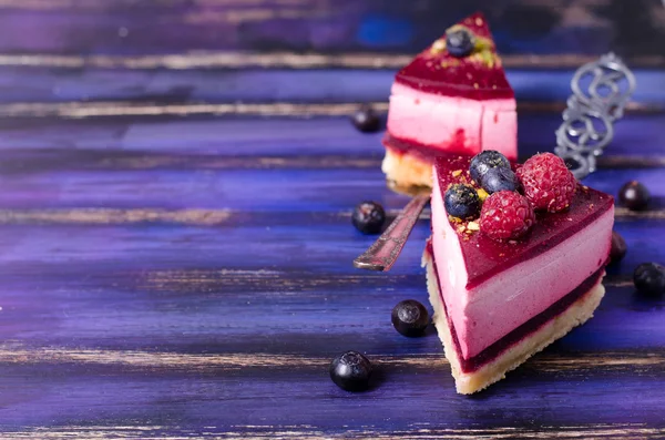 Stuk heerlijke frambozen cake met verse frambozen, bosbessen, krenten en pimpernoten (pistaches) op de schop, helder paars, violet, blauwe achtergrond. Vrije ruimte voor uw tekst. — Stockfoto