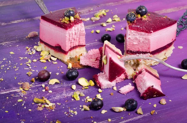 Stuk heerlijke frambozen cake met verse frambozen, bosbessen, krenten en pimpernoten (pistaches) op de schop, lichte paars, violet achtergrond. Vrije ruimte voor uw tekst. — Stockfoto