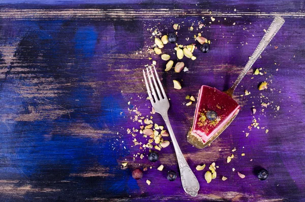 Taze ahududu, yaban mersini, kuş üzümü ve fıstık kürek, parlak mor, mor, mavi arka plan ile lezzetli frambuazlı pasta parçası. Metniniz için boş alan.