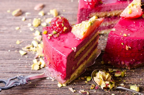 Stuk van heerlijke frambozen taart met verse aardbeien, frambozen, bosbessen, krenten en pimpernoten (pistaches) op de schop, houten achtergrond. Vrije ruimte voor uw tekst. — Stockfoto