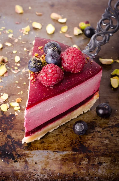 Stuk heerlijke frambozen cake met verse frambozen, bosbessen, krenten en pistachenoten op schop, zwarte achtergrond. Vrije ruimte voor uw tekst. — Stockfoto