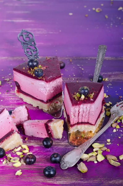 Darab finom torta málna friss málna, áfonya, ribizli és a pisztácia a lapátot, világos lila, lila háttér. Szabad hely a szöveg. — Stock Fotó