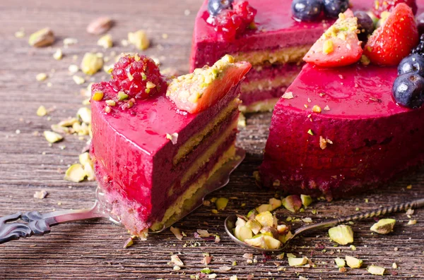 Stuk van heerlijke frambozen taart met verse aardbeien, frambozen, bosbessen, krenten en pimpernoten (pistaches) op de schop, houten achtergrond. Vrije ruimte voor uw tekst. — Stockfoto