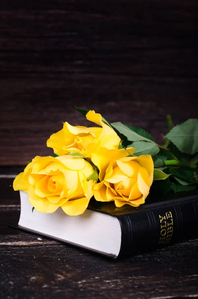 Yellow roses laying on a Bible, wooden background. Free space for your text