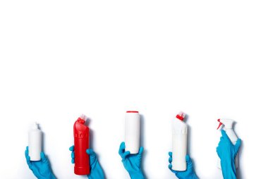 Mavi eldivenli eller beyaz arka planda deterjan şişeleri tutuyor. Fotokopi alanı olan pankart. Kimyasal ürünler, ev kimyasalları, fırçalar ve malzeme kolajı. Temizlik hizmeti kavramı.