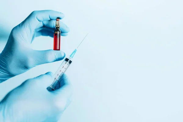 İlaç, iğne ve aşı konsepti. Mavi arka planda şırınga ve ampul tutan tıbbi eldivenler. Uzayı kopyala Karantina Coronavirus salgını sırasında sağlık ekipmanları.