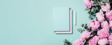 Not defteri, pembe şakayık, mavi arka planda okaliptüs çiçeği olan kadınsı çalışma alanı. Üst görünüm, boşluğu kopyala. Blogcu, kadınsı iş konsepti. Düz yatıyordu. Doğum günü, Kadın Günü. Model.