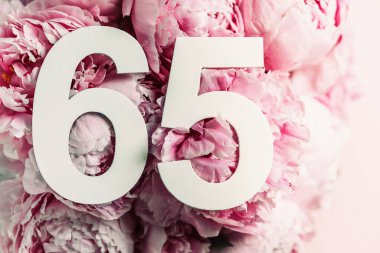 Şakayık çiçekleri, altmış beş basamaklı. Altmış beş yazılı doğum günü tebrik kartı. Yıldönümü konsepti. Üst Manzara. Çiçek arka planında beyaz numara. Sayısal rakam, kutlama olayı, şablon, broşür.