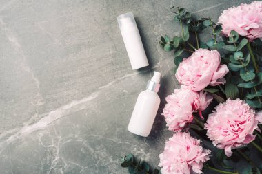 Kozmetik krem şişesi, pembe şakayık çiçekleri, okaliptüs çiçeği, mermer arka planda kopya alanı. Marka modeli için boş etiket. Düz yatıyordu. Güzellik ürünleri. Cilt bakımı, vücut bakımı, spa konsepti.
